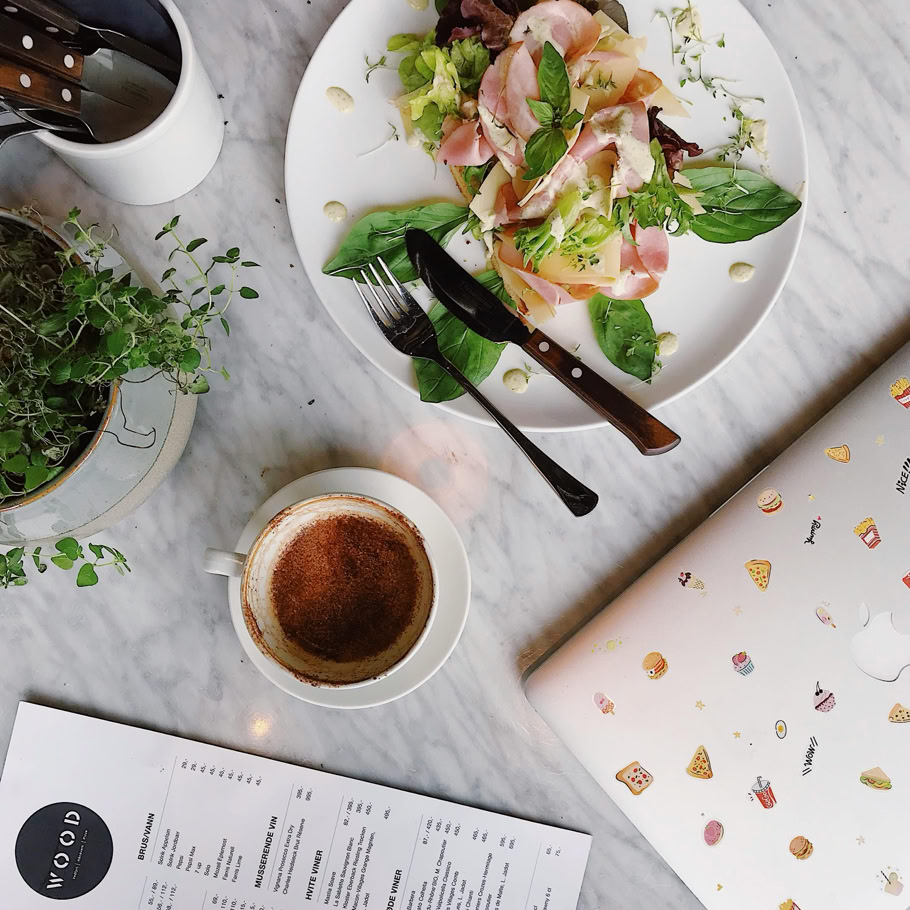 Top view of an elegant breakfast setup featuring coffee, fresh salad, and a laptop over a marble table.