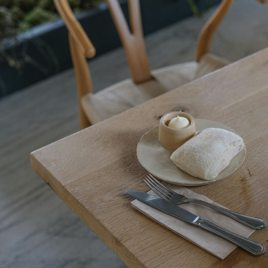 A minimalist breakfast setup with ciabatta and butter on a modern wooden table.